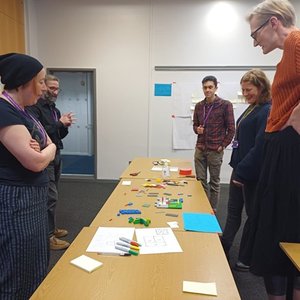 Five people standing round a desk looking at some lego