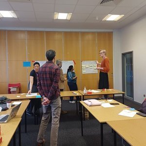 Five people standing in amongst a U shape of desks looking at the wall or the desk