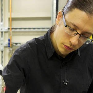 Photo of Russell. He has dark hair and is looking down to his left,  wearing frameless glasses and a black shirt.