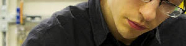 Photo of Russell. He has dark hair and is looking down to his left,  wearing frameless glasses and a black shirt.