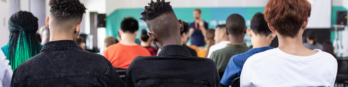 Photo of a group of young college students from behind looking at a teacher