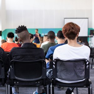 Photo of a group of young college students from behind looking at a teacher