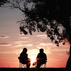 A couple sitting on camping chairs chatting whilst the sunsets
