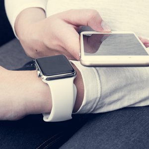 man in a white long sleeved top wearing a white apple watch holding an iPhone next to it on his left wrist